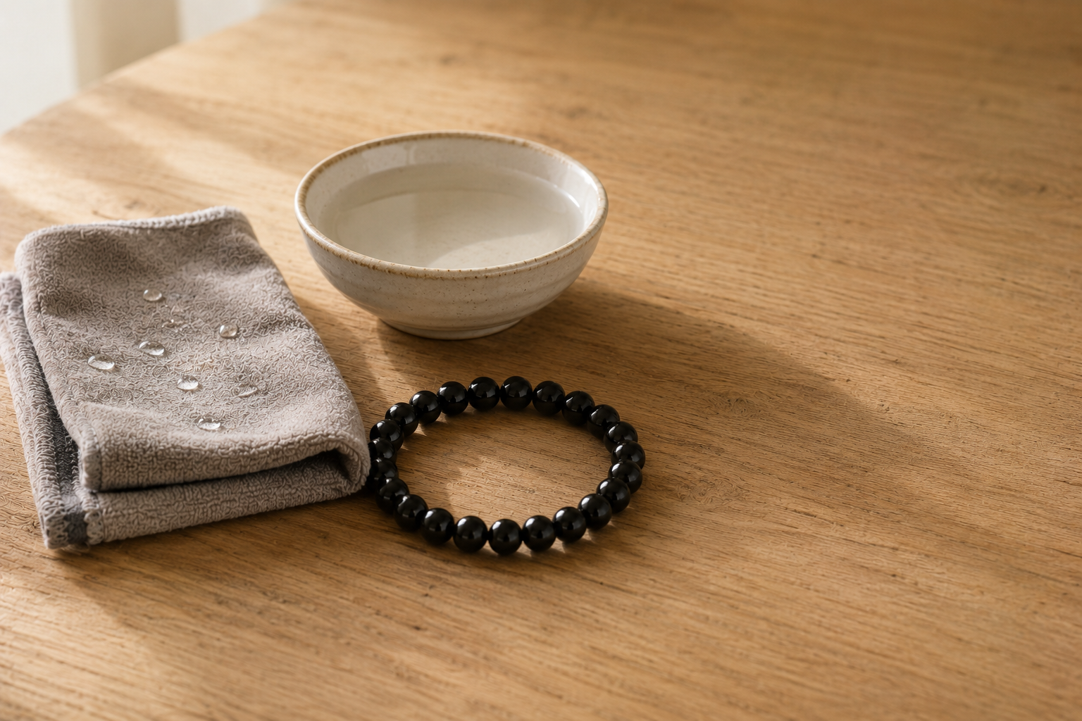 Un bijou en obsidienne est il fragile ? La réponse d'une créatrice Chiffon doux humide et bracelet d obsidienne noire pres d une coupelle d eau