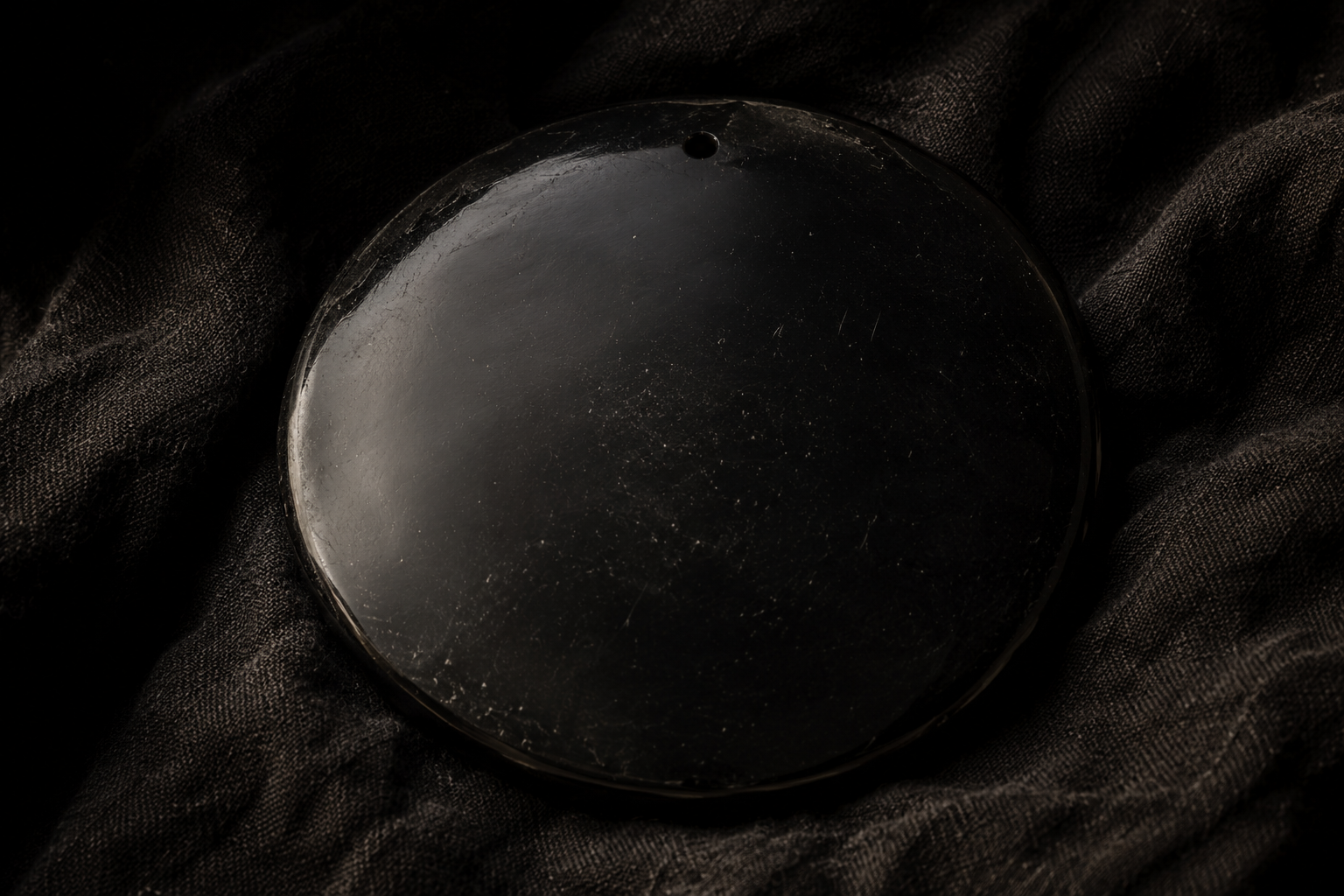 Miroir circulaire en obsidienne polie posé sur une étoffe sombre