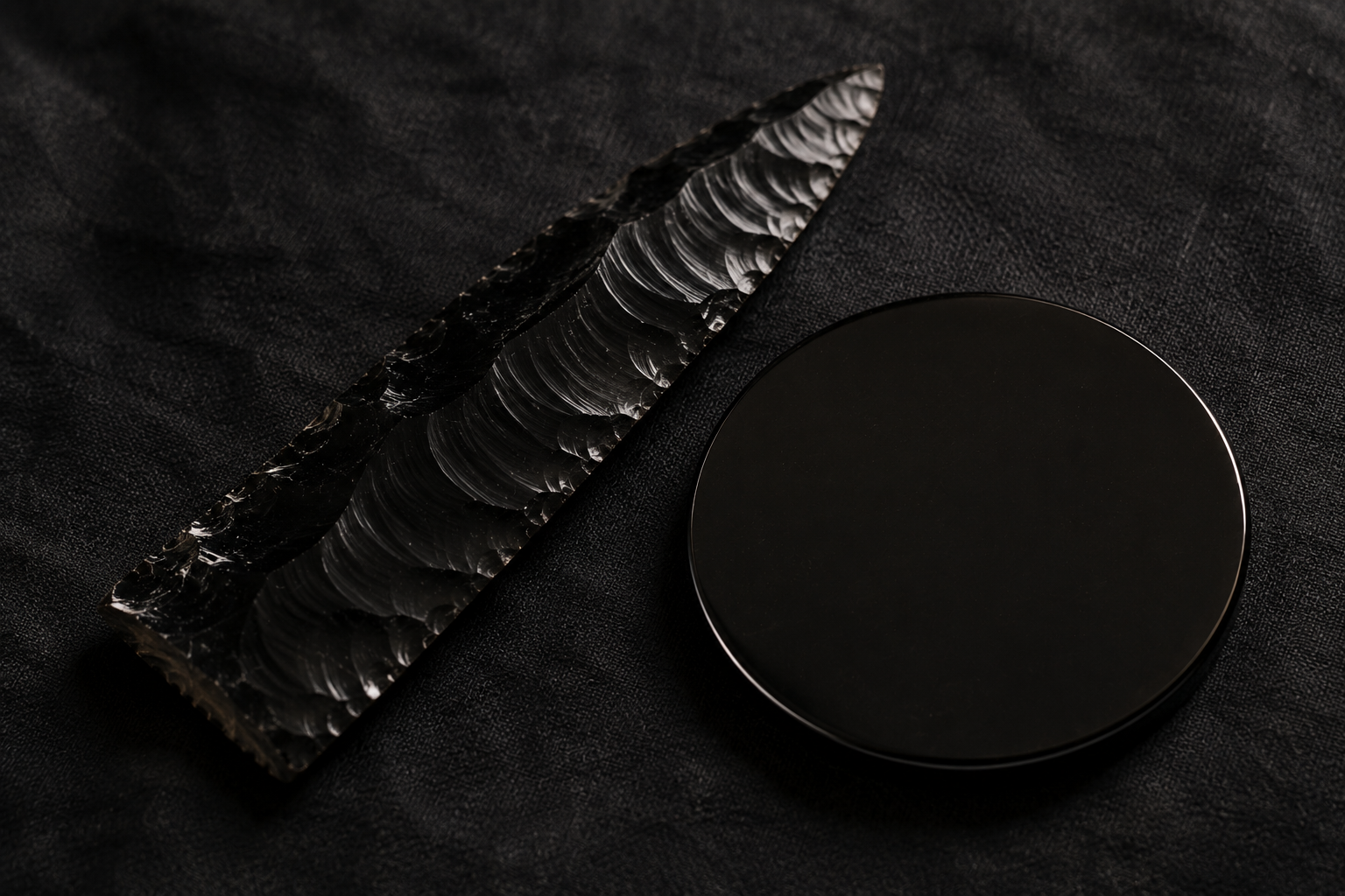 Black obsidian blade and disc resting on dark fabric