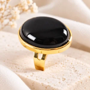 Grosse bague dorée ajustable portant un cabochon rond d'obsidienne noire dans une large bordure