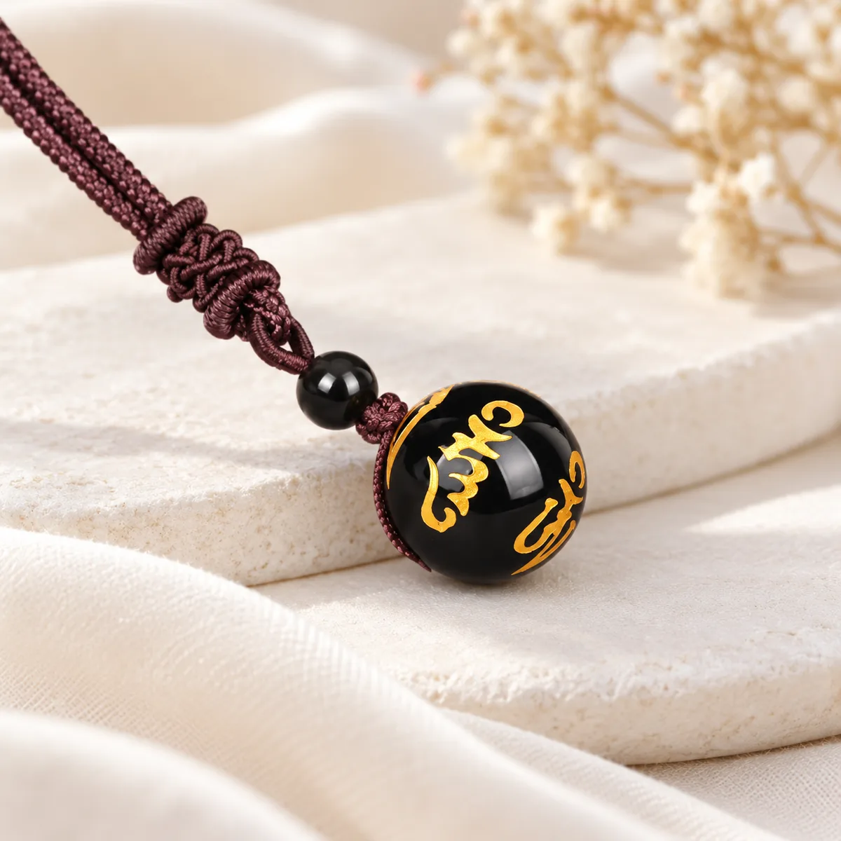 Pendentif boule mantra obsidienne Pendentif en boule d'obsidienne gravée du mantra tibétain rehaussé d'or